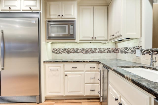 kitchen with dark stone countertops, sink, built in appliances, and backsplash