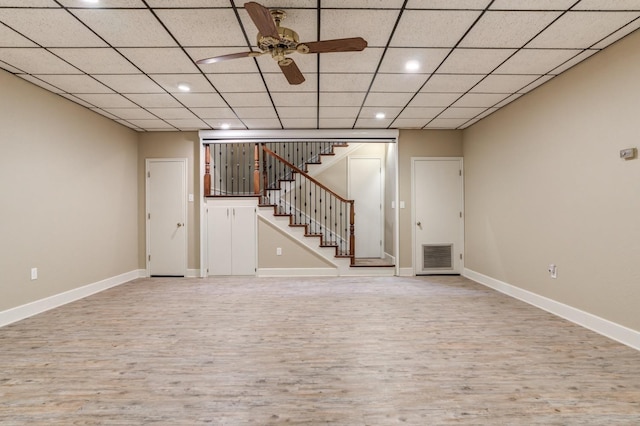 basement featuring ceiling fan, a drop ceiling, and light wood-type flooring