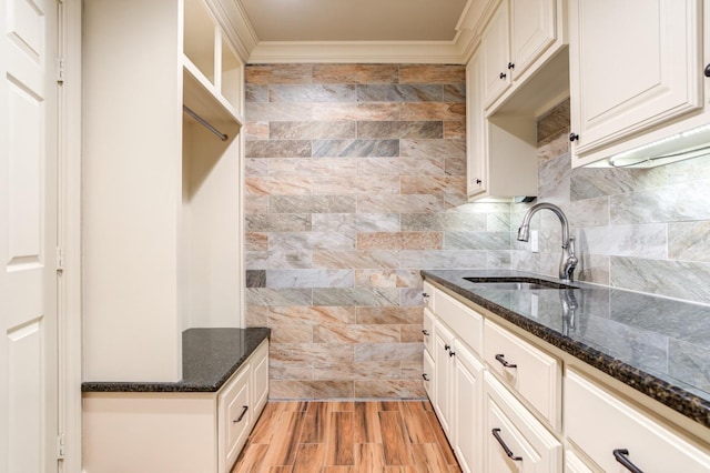 kitchen with sink, crown molding, dark stone countertops, light hardwood / wood-style floors, and white cabinets