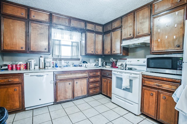 kitchen with light tile patterned flooring, sink, a textured ceiling, and white appliances