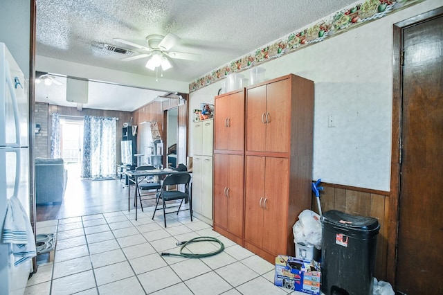 kitchen featuring ceiling fan, wooden walls, a textured ceiling, and stainless steel refrigerator