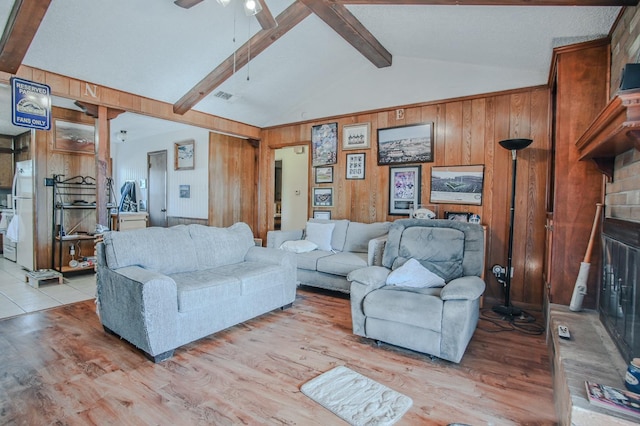 living room with wooden walls, lofted ceiling with beams, ceiling fan, and light wood-type flooring