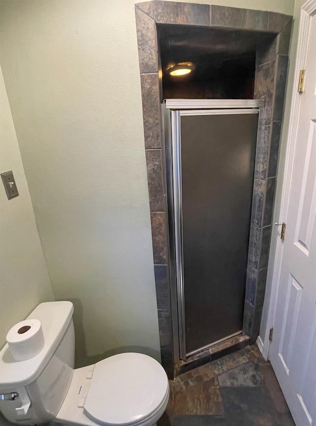 bathroom featuring a shower with shower door and toilet