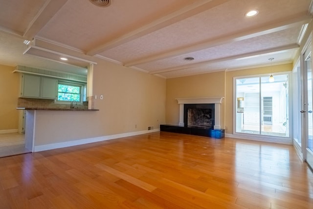 unfurnished living room featuring beamed ceiling, ornamental molding, and light hardwood / wood-style flooring