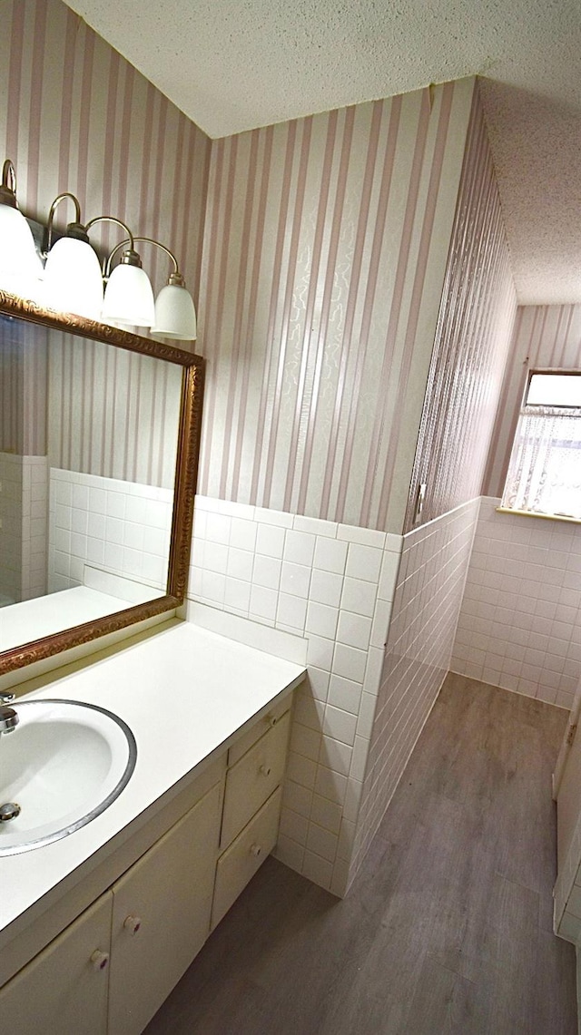 bathroom featuring vanity, wood-type flooring, tile walls, and a textured ceiling