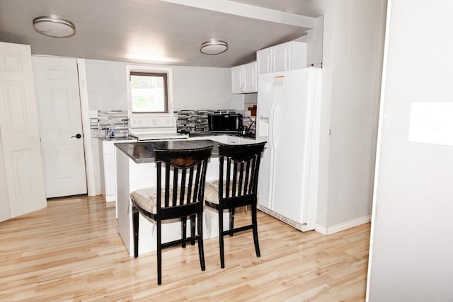 kitchen featuring a kitchen bar, light hardwood / wood-style flooring, white appliances, decorative backsplash, and white cabinets