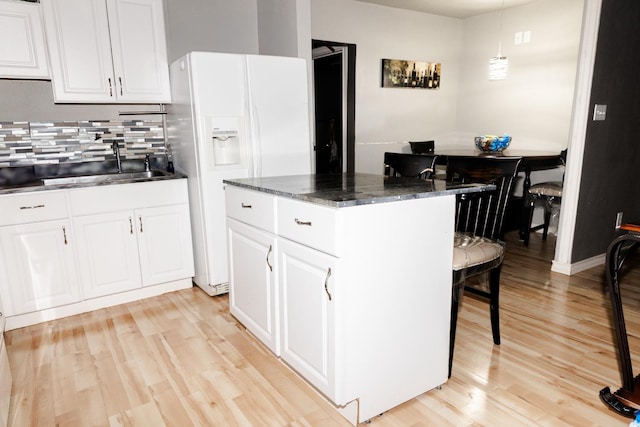 kitchen featuring white refrigerator with ice dispenser, sink, hanging light fixtures, and white cabinets