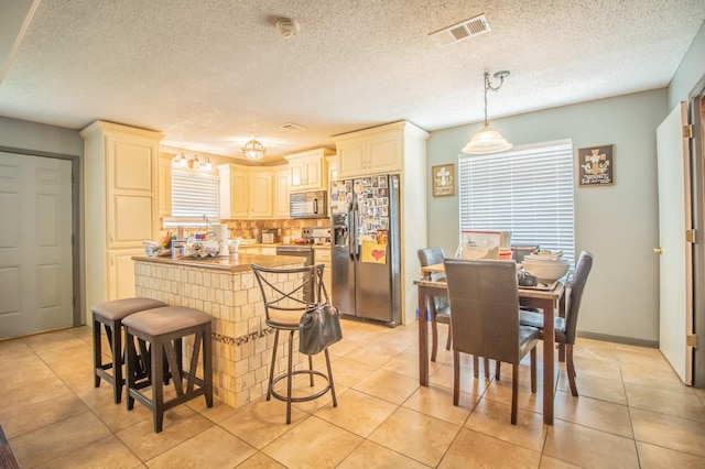 kitchen featuring pendant lighting, backsplash, stainless steel appliances, cream cabinets, and a kitchen bar