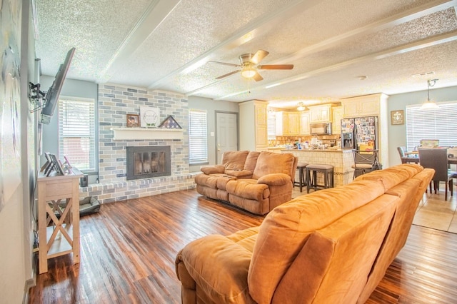 living room featuring a brick fireplace, beam ceiling, light hardwood / wood-style floors, and a textured ceiling