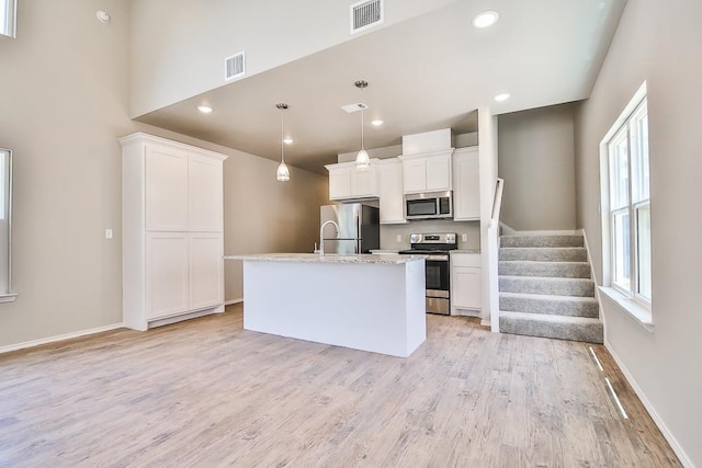 kitchen with a kitchen island with sink, hanging light fixtures, white cabinets, and appliances with stainless steel finishes