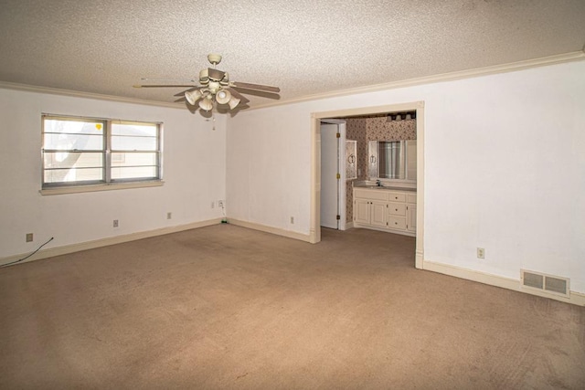 empty room featuring ceiling fan, light colored carpet, ornamental molding, and a textured ceiling