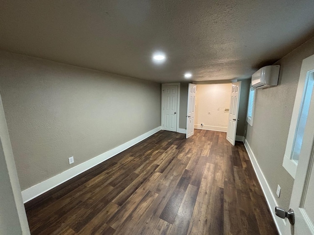 basement featuring an AC wall unit, dark wood-type flooring, and a textured ceiling