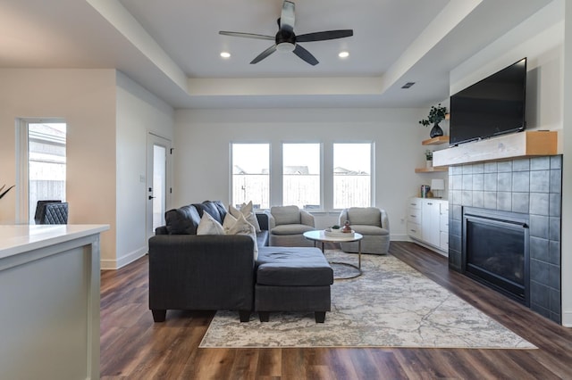 living room featuring a tile fireplace, plenty of natural light, dark wood-style flooring, and a tray ceiling