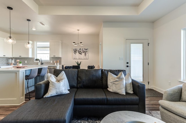 living area featuring visible vents, an inviting chandelier, a tray ceiling, and dark wood-type flooring
