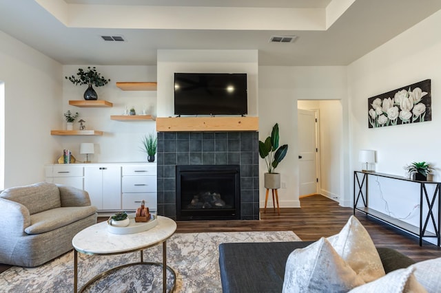 living area featuring a tile fireplace, wood finished floors, visible vents, and baseboards
