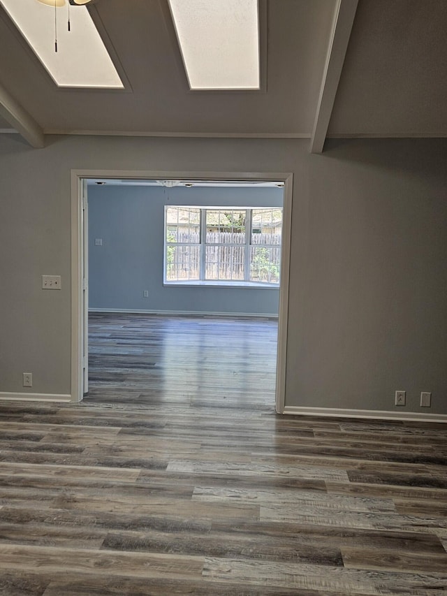 empty room featuring a skylight, dark wood-type flooring, beam ceiling, and baseboards