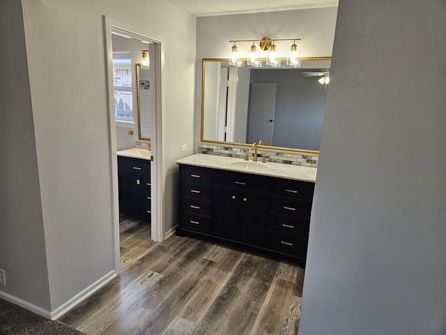 bathroom with tasteful backsplash, wood finished floors, vanity, baseboards, and a ceiling fan