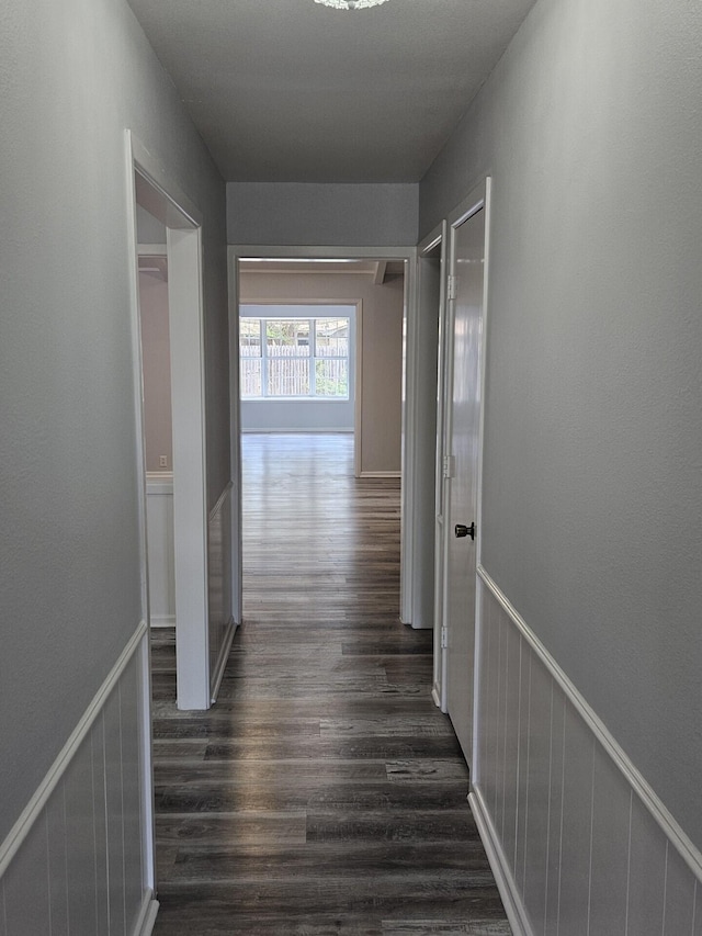 corridor with dark wood-type flooring and a wainscoted wall