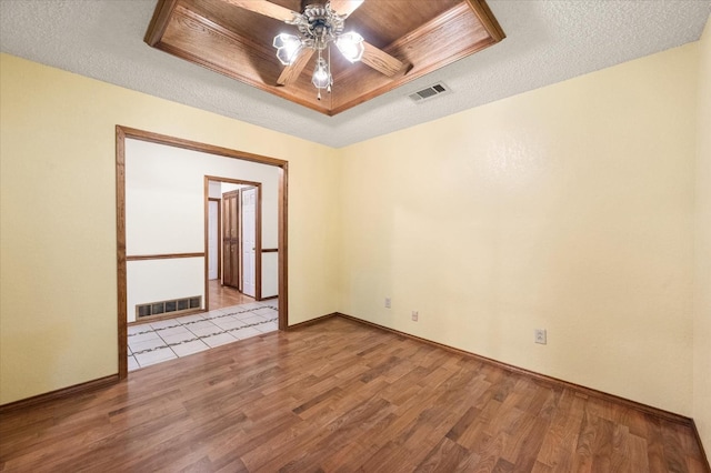 unfurnished room with ceiling fan, light hardwood / wood-style flooring, a textured ceiling, and a tray ceiling