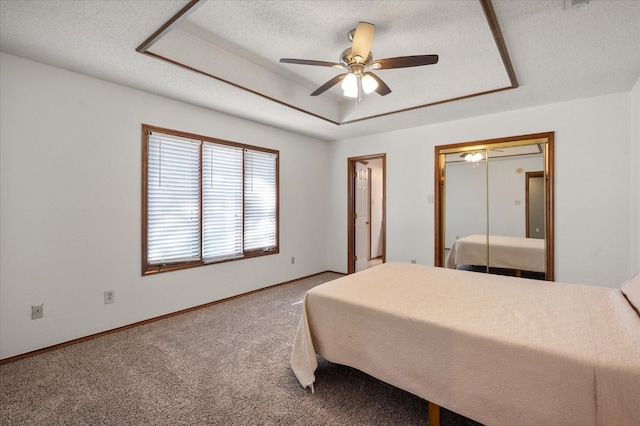 bedroom with a textured ceiling, a raised ceiling, a closet, ceiling fan, and carpet