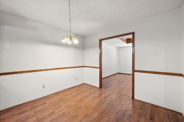 unfurnished room featuring hardwood / wood-style floors, a notable chandelier, and a textured ceiling