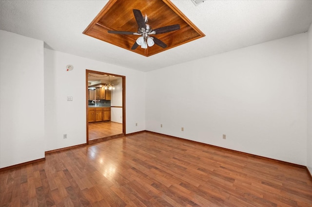 empty room with sink, a tray ceiling, wood-type flooring, and ceiling fan with notable chandelier