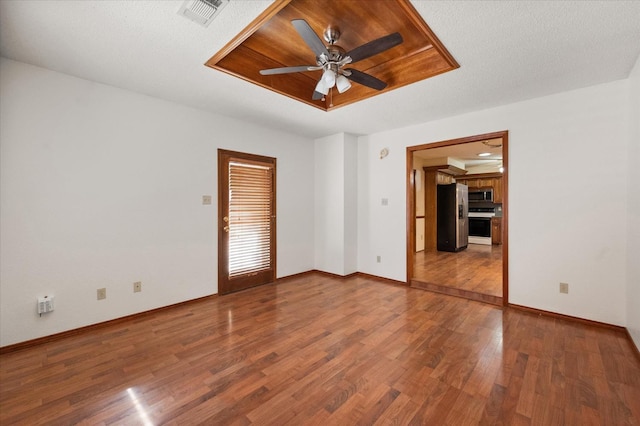 empty room with hardwood / wood-style floors, a textured ceiling, a raised ceiling, and ceiling fan