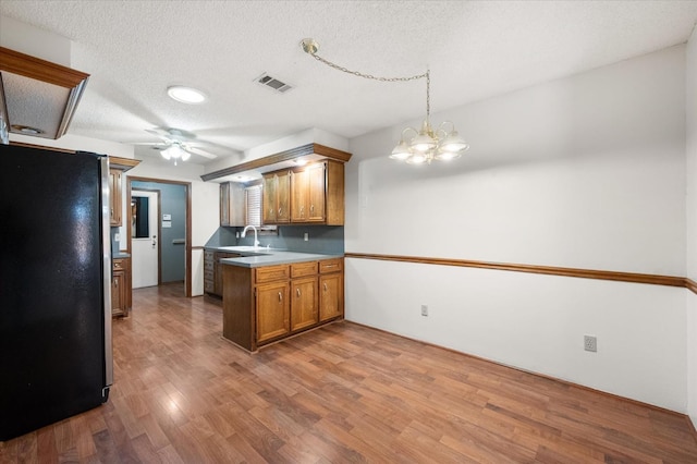 kitchen featuring stainless steel refrigerator, sink, hanging light fixtures, kitchen peninsula, and light wood-type flooring