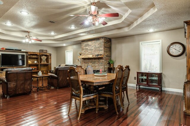 dining space with ceiling fan, a tray ceiling, dark hardwood / wood-style floors, and a textured ceiling