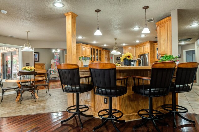 bar featuring decorative columns, decorative light fixtures, a textured ceiling, and stainless steel fridge with ice dispenser