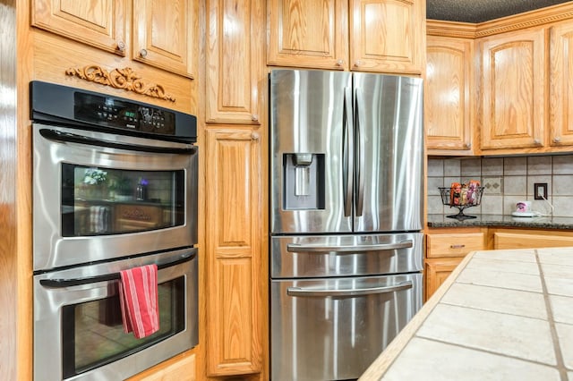 kitchen with appliances with stainless steel finishes, tile countertops, light brown cabinetry, and decorative backsplash