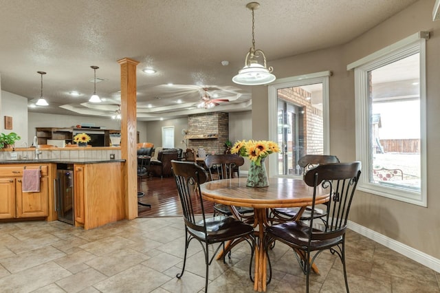 dining space featuring sink, ceiling fan, wine cooler, a textured ceiling, and a brick fireplace