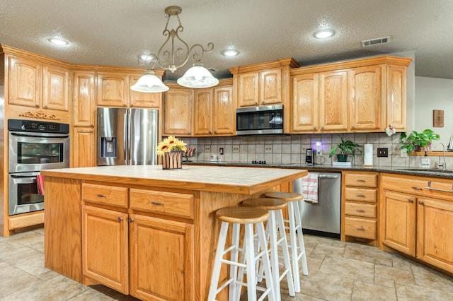 kitchen featuring a kitchen island, appliances with stainless steel finishes, sink, backsplash, and hanging light fixtures