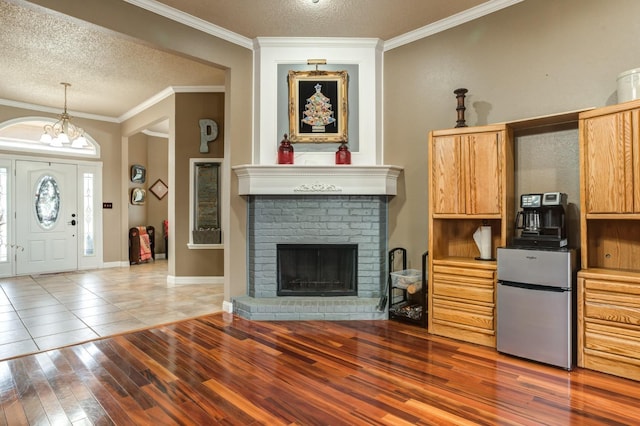 kitchen with a fireplace, stainless steel fridge, hardwood / wood-style flooring, crown molding, and a textured ceiling