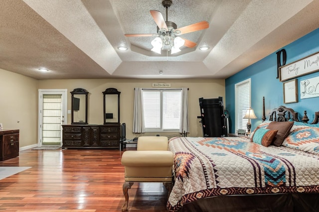 bedroom with ceiling fan, hardwood / wood-style flooring, a raised ceiling, and a textured ceiling