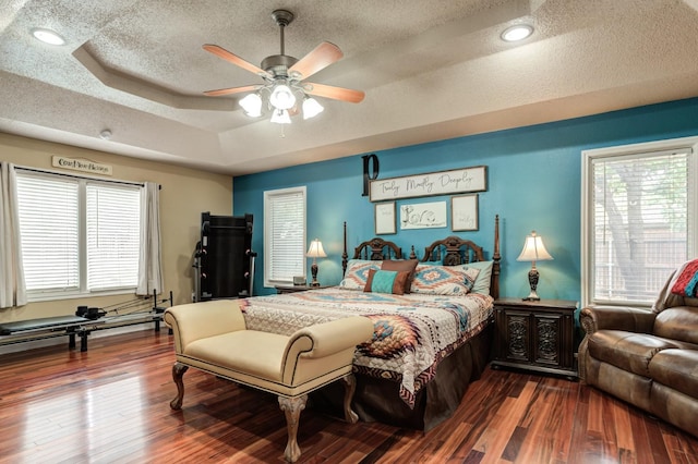 bedroom with multiple windows, a tray ceiling, wood-type flooring, and a textured ceiling