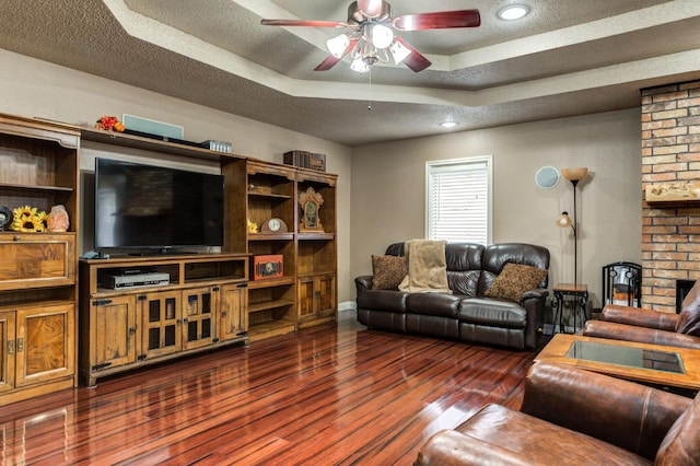 living room with dark wood-type flooring, ceiling fan, a tray ceiling, and a textured ceiling