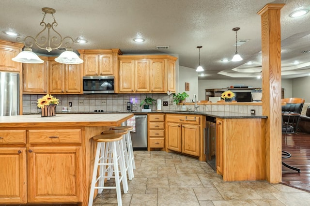 kitchen featuring sink, a breakfast bar, appliances with stainless steel finishes, hanging light fixtures, and kitchen peninsula