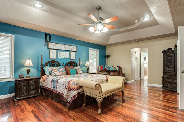 bedroom featuring multiple windows, hardwood / wood-style flooring, a raised ceiling, and a textured ceiling