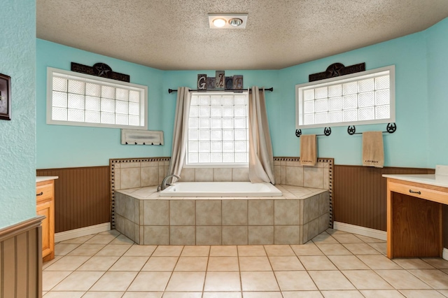 bathroom with tiled tub, vanity, tile patterned flooring, and a textured ceiling