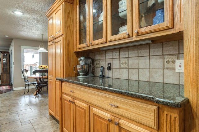 kitchen with tasteful backsplash, dark stone counters, hanging light fixtures, and a textured ceiling