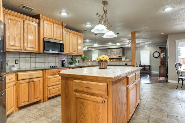 kitchen featuring pendant lighting, ceiling fan, a center island, tasteful backsplash, and tile countertops