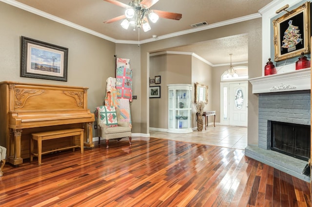 sitting room featuring hardwood / wood-style flooring, ornamental molding, a textured ceiling, a brick fireplace, and ceiling fan with notable chandelier