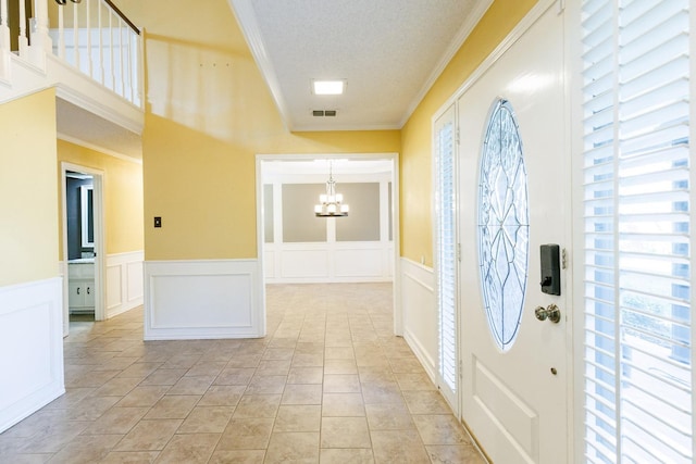 tiled foyer with crown molding, a textured ceiling, and a chandelier