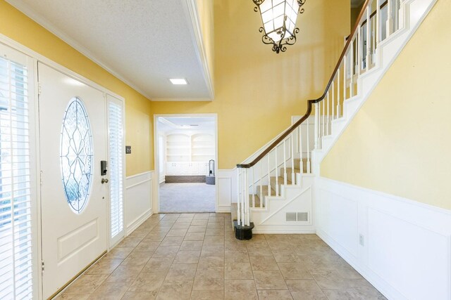 tiled foyer featuring ornamental molding, a chandelier, a textured ceiling, and a wealth of natural light