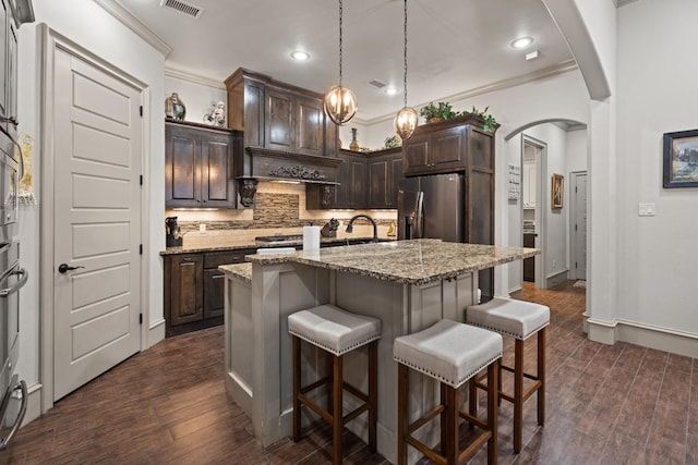 kitchen with hanging light fixtures, dark brown cabinets, a kitchen island with sink, and stainless steel fridge with ice dispenser