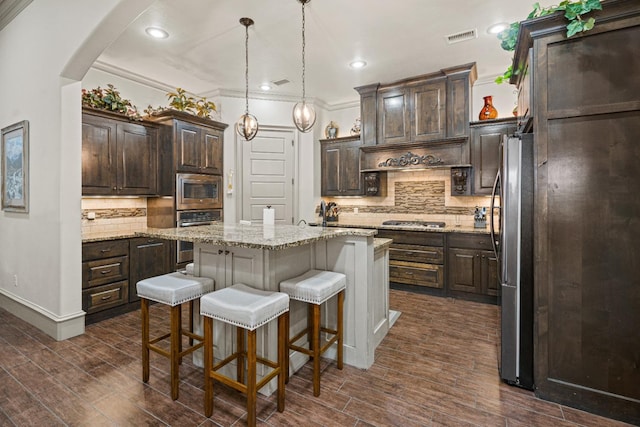 kitchen featuring dark wood-type flooring, dark brown cabinets, hanging light fixtures, appliances with stainless steel finishes, and a kitchen island