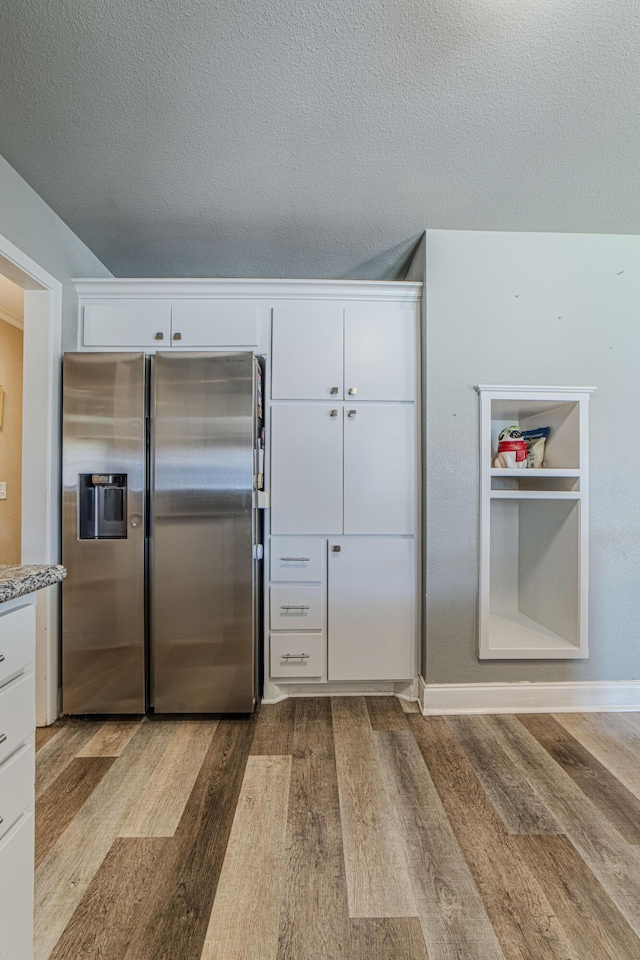 kitchen featuring stainless steel refrigerator with ice dispenser, white cabinetry, light wood finished floors, and a textured ceiling