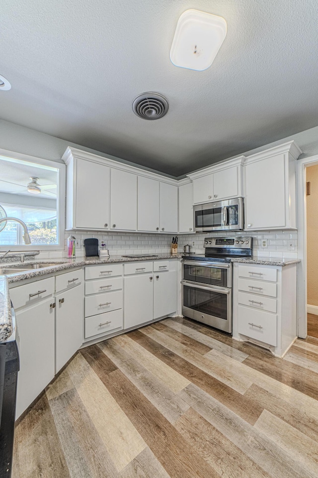 kitchen with stainless steel appliances, light wood-style floors, white cabinets, backsplash, and a sink