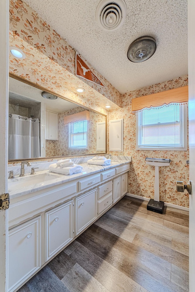 full bath with visible vents, wood finished floors, wallpapered walls, and a sink